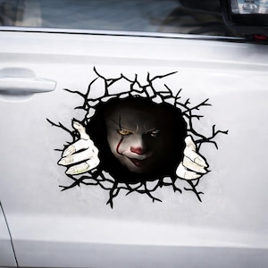 May include: A white car door with a decal featuring a scary clown face peering through a hole. The clown has white skin, red accents, and yellow eyes. The decal is designed to look like the car door is breaking apart.