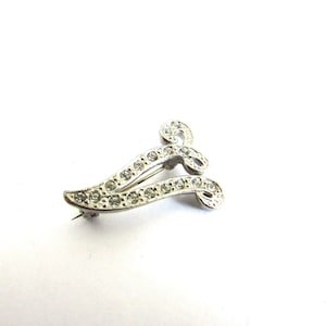 May include: A silver brooch with a swirling design, accented with clear rhinestones.