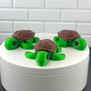 May include: Three small turtle figurines with bright green bodies and brown shells. Each turtle features a smooth, rounded head with dark, circular eyes and articulated limbs. The figures are arranged in a cluster, showcasing their detailed, textured shell patterns and vibrant, solid-colored plastic construction.