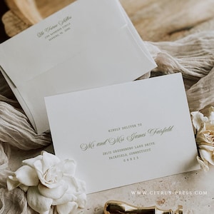 Op de afbeelding: Elegante trouwuitnodigingsset met witte enveloppen en een kaart met de tekst "Kindly Deliver To". Een gouden lakzegel en witte bloemen zijn ook aanwezig. De website www.citrus-press.com is zichtbaar.