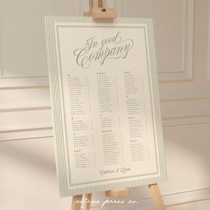 Puede incluir: Un plano de asientos color crema con las palabras "In good Company" en una elegante escritura. El gráfico está enmarcado con finas rayas verticales y descansa sobre un caballete de madera. Los nombres están listados alfabéticamente.