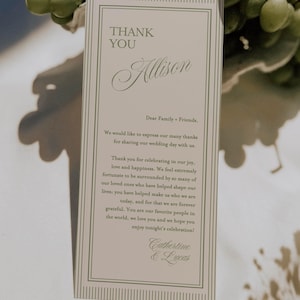 Puede incluir: Tarjeta de agradecimiento de boda con el nombre "Allison" en escritura cursiva. La tarjeta tiene un borde verde claro y un mensaje de agradecimiento de Catherine y Lucas. Uvas verdes en el fondo.