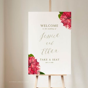 May include: A white wedding welcome sign with pink flowers and green leaves. The sign reads "Welcome to the wedding of Jessica and Ethan. Take a seat, not a side."
