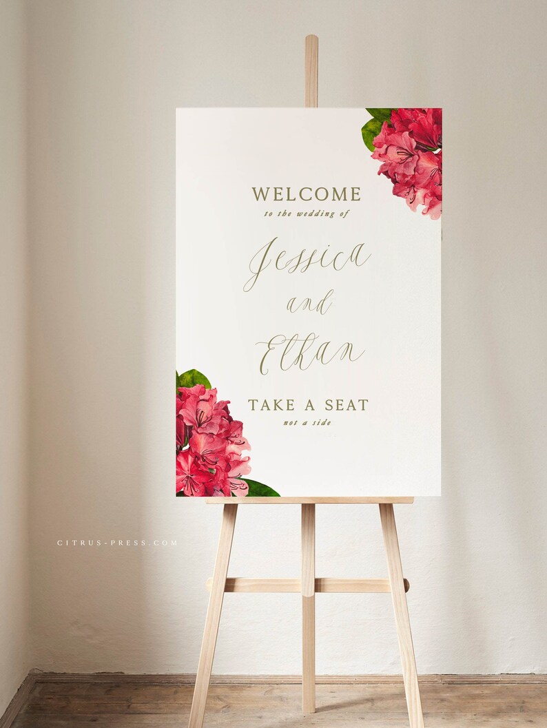 May include: A white wedding welcome sign with pink flowers and green leaves. The sign reads "Welcome to the wedding of Jessica and Ethan. Take a seat, not a side."