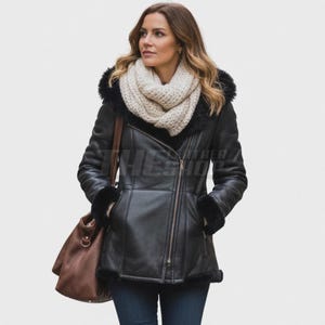 Puede incluir: Chaqueta de cuero negra con capucha y puños forrados de piel sintética. La chaqueta tiene una cremallera diagonal y un bolso de hombro marrón. Una bufanda color crema se lleva alrededor del cuello.