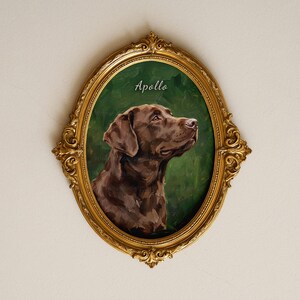 Puede incluir: Un marco dorado ornamentado de forma ovalada que contiene un retrato pintado de un perro labrador retriever marrón sobre un fondo verde oscuro. El nombre Apollo está escrito en letra cursiva blanca sobre la cabeza del perro.
