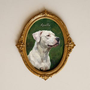 Puede incluir: Un marco ovalado dorado y ornamentado que contiene una pintura al óleo de un perro blanco sobre un fondo verde oscuro. El nombre Apollo está escrito en letra blanca sobre la cabeza del perro. El marco presenta detalles intrincados en relieve.