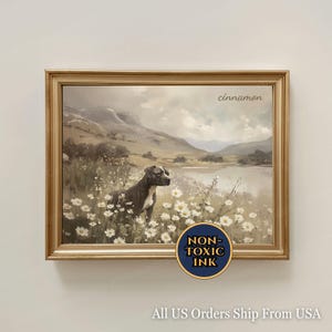 May include: Framed artwork featuring a dog in a field of white flowers with a lake and mountains in the background. The artwork has a gold frame and the word "cinnamon" is written in the upper right corner. A blue and gold sticker reads "NON-TOXIC INK".