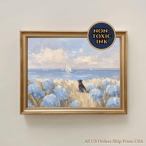 May include: A framed landscape painting featuring a black dog sitting in a field of light blue flowers and tall grass, looking out at a calm blue sea with sailboats under a cloudy sky. A circular badge in the corner reads NON-TOXIC INK.