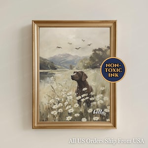 Peut inclure: Impression sur toile encadrée d'un chien marron dans un champ de marguerites blanches, avec des montagnes et un lac en arrière-plan. L'œuvre d'art est encadrée d'or, avec le mot "bella". Un autocollant circulaire indique "NON-TOXIC INK".