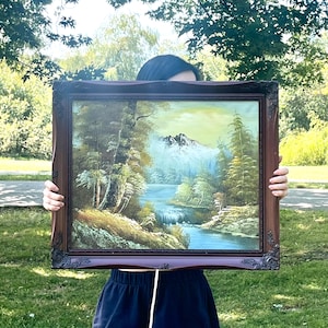 以下が含まれることがあります： 暗い茶色の装飾的な木製フレームに入った風景画。滝と木々のある山のシーンが描かれています。絵画は青、緑、白を使用して、穏やかなシーンを作り出しています。フレームは、さまざまなインテリアスタイルに適したクラシックなデザインです。