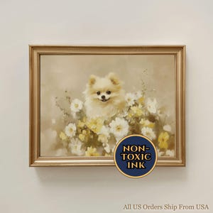 Pode incluir: Uma pintura emoldurada de um cão Pomerânia fofo, cor creme, rodeado por flores brancas e amarelas. A obra de arte tem um estilo suave e pictórico com uma moldura dourada. Um autocolante circular azul e dourado diz "NON-TOXIC INK".