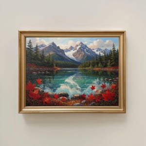 May include: A framed landscape painting depicts a serene lake reflecting snow-capped mountains and a blue sky. Red maple leaves and rocks frame the foreground. The artwork is encased in a gold-colored frame.