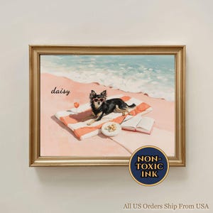 Op de afbeelding: Een ingelijste kunstdruk toont een zwart-tan Chihuahua met een zonnebril, liggend op een strandlaken met een drankje en snacks. Het kunstwerk is geplaatst op een roze strand met een blauwe oceaan en lucht. Het woord "daisy" staat op de kunst.