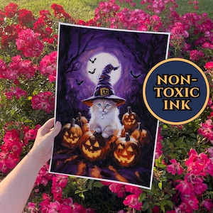 Op de afbeelding: Een Halloween-print met een witte kat met een heksenhoed, zittend op uitgekerfde pompoenen. De achtergrond toont een volle maan, vleermuizen en een donker bos. De print heeft een cirkelvormig "NON-TOXIC INK" logo.
