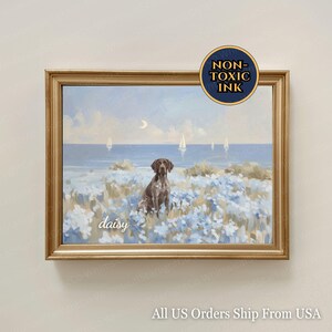 Op de afbeelding: Een ingelijste print met een bruine hond die in een veld met blauwe bloemen zit, met een achtergrond van een zeegezicht. Het kunstwerk heeft een gouden lijst en het woord "daisy" staat op de print. De print is gelabeld "Non-Toxic Ink".