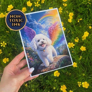 May include: A rectangular print featuring a white fluffy dog with large rainbow-colored wings standing on a stone bridge. The background shows a blue sky with clouds and a rainbow. A circular badge on the print contains the text NON-TOXIC INK.