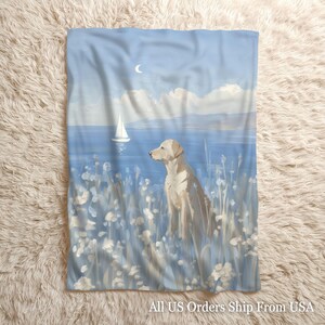May include: A rectangular throw blanket featuring a printed illustration of a light-colored dog sitting in a field of white flowers. The background depicts a blue ocean, a white sailboat on the water, a crescent moon, and a soft cloudy sky.
