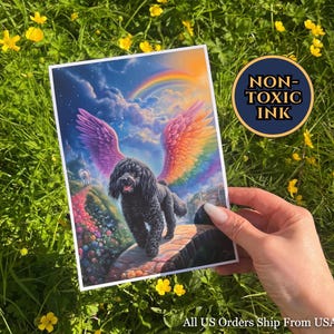 Op de afbeelding: Een print met een zwarte poedel met regenboogvleugels, tegen een achtergrond van een regenboog en een kleurrijk landschap. De print heeft de tekst "NON-TOXIC INK" in een cirkelvormig ontwerp.