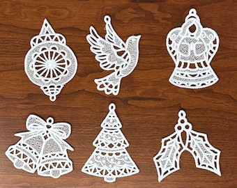 May include: Six white lace Christmas decorations, including a bell, a dove, a tree, a holly sprig, an angel, and a traditional bauble.