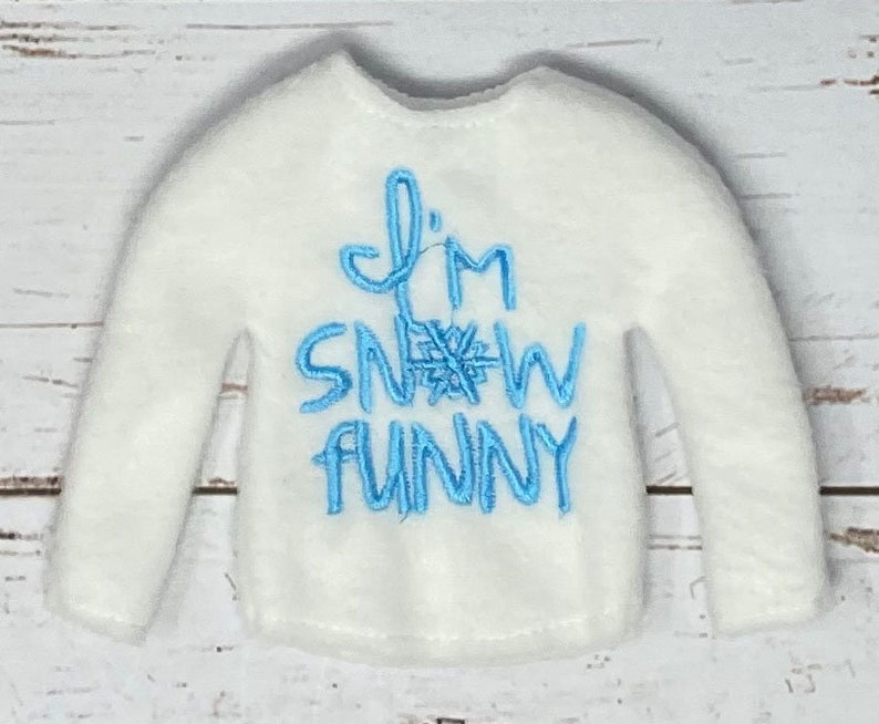 K&ouml;nnte beinhalten: Wei&szlig;es Langarmshirt mit blau gesticktem Text "I'm Snow Funny" und einer Schneeflocke.