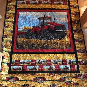 May include: A red and black tractor quilt featuring a large image of a red tractor in the centre. The quilt is made of fabric squares with images of tractors and the words "CASE IH" repeated throughout.
