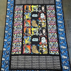 Könnte beinhalten: Eine schwarz-weiße Steppdecke mit Star Wars-Motiv. Die Steppdecke zeigt ein Raster mit Bildern von Star Wars-Charakteren, darunter Yoda, Darth Vader, Chewbacca und Luke Skywalker. Die Steppdecke ist von einem blauen Rand mit einem sich wiederholenden Muster von Raumschiffen umgeben.