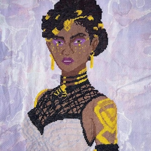 May include: Cross-stitch embroidery of a woman with dark skin, wearing a white dress with black and gold accents. Her hair is styled in a bun with gold accents. She has purple eyeshadow and gold earrings.
