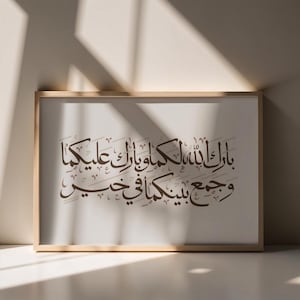 Op de afbeelding: Een ingelijste print met elegante Arabische kalligrafie in donkerbruin schrift op een crèmekleurige achtergrond. De houten lijst heeft een lichtbruine afwerking. Het kunstwerk wordt getoond tegen een neutrale muur met schaduwen.