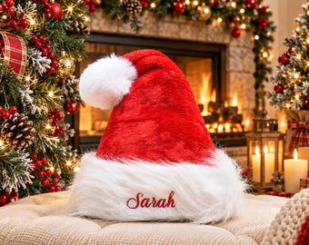 May include: A plush red Santa hat featuring a white faux fur trim and a white pom-pom at the tip. The white trim is embroidered with the name Sarah in red script lettering. The hat is made of a soft, fuzzy material and has a classic conical shape.
