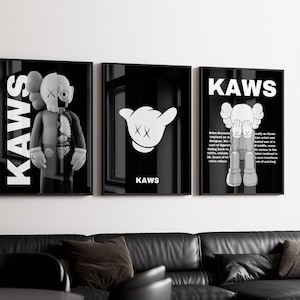 May include: Three black and white framed prints with the word "KAWS" in white text. The left print features a black and white illustration of a character with an X for eyes. The middle print features a black and white illustration of a character with an X for eyes and the word "KAWS" in white text. The right print features a black and white illustration of a character with an X for eyes and the word "KAWS" in white text. The print also includes text about the artist.