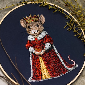 Op de afbeelding: Een geborduurd kunstwerk met een koninklijke muis met een kroon en een rode mantel met witte randen. Het ontwerp staat op een donkerblauwe achtergrond in een houten borduurring. De borduursels tonen gedetailleerde steken en hebben een speels thema.