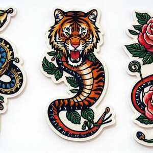 Puede incluir: Tres diseños de pegatinas con ilustraciones estilo tatuaje. Uno muestra una serpiente azul enrollada alrededor de una espada, otro un tigre con la boca abierta y el último una serpiente roja con dos rosas.