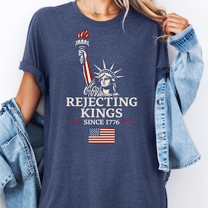 May include: Navy blue t-shirt featuring the Statue of Liberty holding a torch, with the text "Rejecting Kings Since 1776" and an American flag graphic. The shirt has short sleeves and a relaxed fit.
