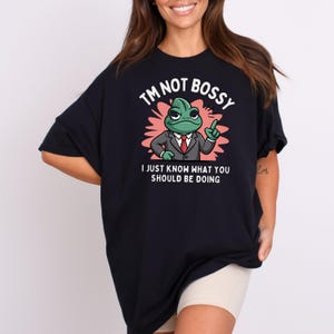 May include: Black oversized t-shirt with a cartoon frog wearing a suit and tie. The text on the shirt reads "I'm not bossy, I just know what you should be doing."