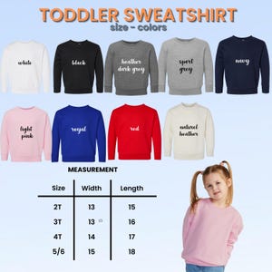 Op de afbeelding: Een selectie van peuter sweatshirts in verschillende kleuren, waaronder wit, zwart, marineblauw en rood. De afbeelding toont ook een maattabel met afmetingen in centimeters, en de tekst "TODDLER SWEATSHIRT".