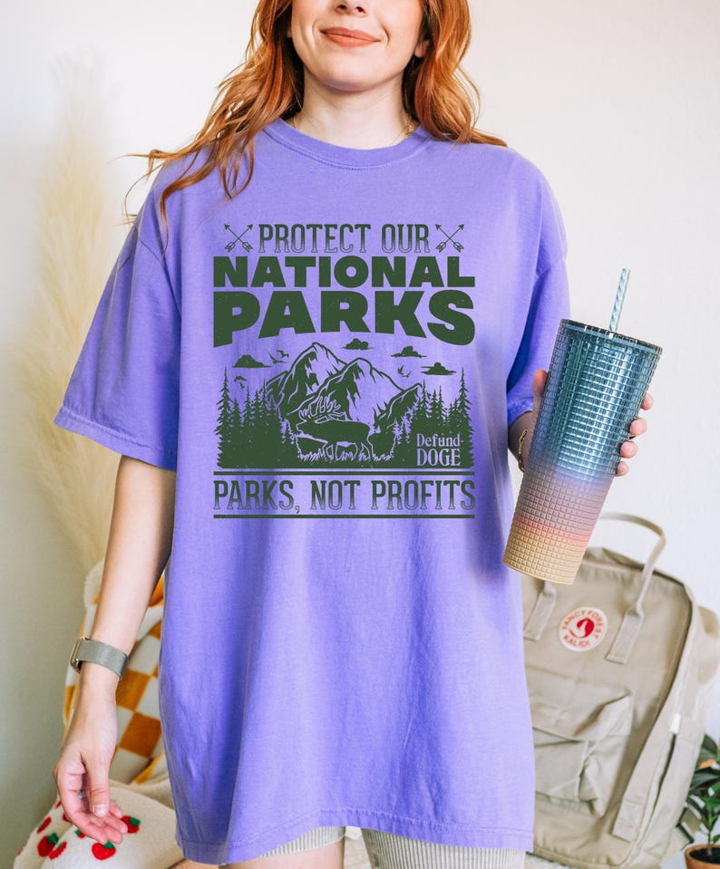 May include: Purple t-shirt with a green graphic that says "Protect Our National Parks" and "Defund Doge" with a mountain scene and the words "Parks, Not Profits".