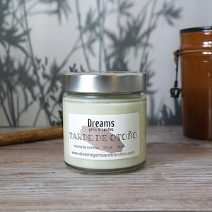 May include: A white soy candle in a glass jar with a silver lid. The label reads "Dreams gems & candles" and "Tarde de Otoño" with the website address "www.dreamsgemsandcandles.com".