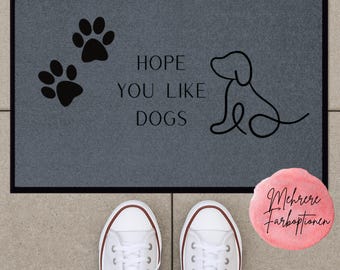 Könnte beinhalten: Eine graue Fußmatte mit schwarzem Rand zeigt Pfotenabdrücke, eine Hundeumrisslinie und den Text "HOPE YOU LIKE DOGS". Weiße Turnschuhe sind unten zu sehen. Ein rosa Kreis mit Text befindet sich rechts.