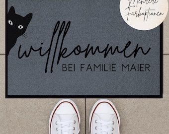 Può includere: Un tappetino di benvenuto grigio con il testo "Willkommen bei Familie Maier" e un gatto nero che spunta da sinistra. Il testo "Mehrere Farboptionen" è scritto in un cerchio in alto a destra.
