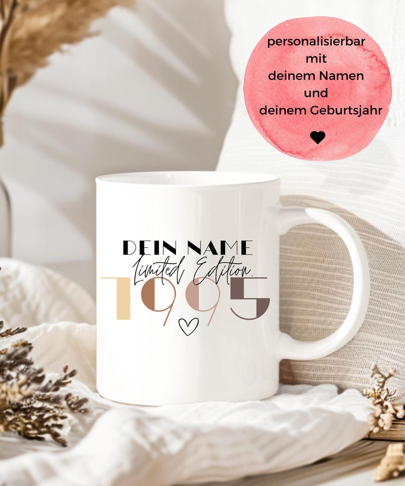 May include: White ceramic mug with black text that reads "Dein Name Limited Edition 1995" with a small heart symbol. The numbers 1, 9, 9, and 5 are in different colors of brown and beige.