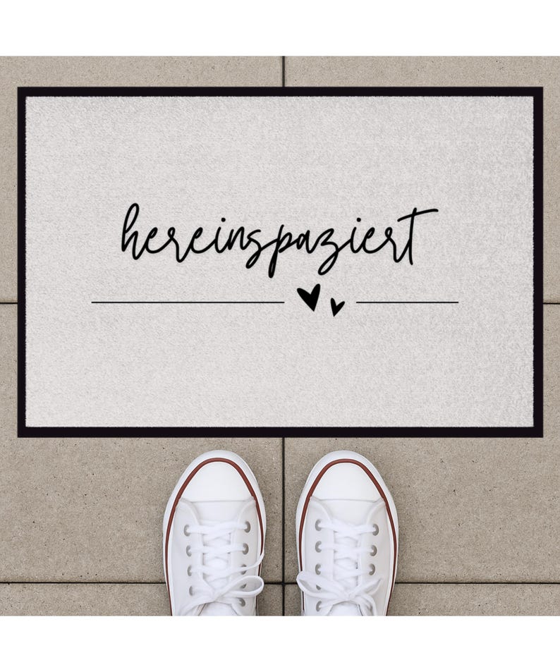 May include: A white doormat with black text that reads "hereinspaziert" with two small black hearts below the text.