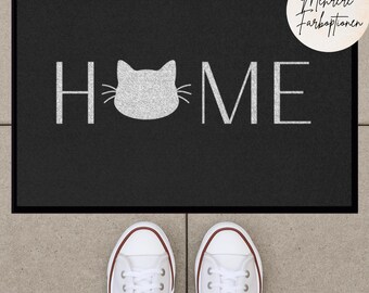 Può includere: Tappetino nero per la porta con la parola "HOME" in lettere bianche e una silhouette di gatto bianca al centro della parola. Il testo "Mehrere Farboptionen" è nell'angolo in alto a destra del tappetino.