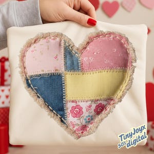 Puede incluir: Un cojín crema con un diseño de corazón de patchwork. El corazón está compuesto por cuadrados de tela en azul vaquero, rosa floral, amarillo y rosa floral, con un borde deshilachado. El cojín lo sostiene una persona con esmalte de uñas rojo.