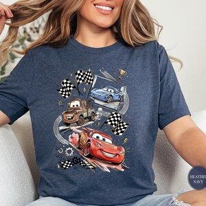 A woman wearing a blue t-shirt with a graphic of two cars racing, one blue and one red, along with checkered flags and other racing elements.