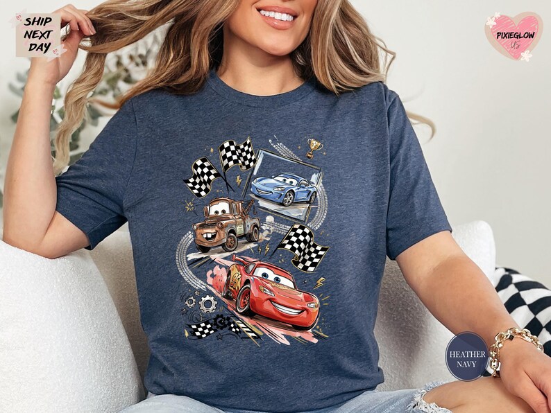 A woman wearing a blue t-shirt with a graphic of two cars racing, one blue and one red, along with checkered flags and other racing elements.