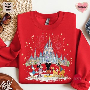 A red sweatshirt with a Disney-themed illustration of Minnie Mouse, Mickey Mouse, Donald Duck, and Goofy standing in front of a castle, with fireworks in the background.