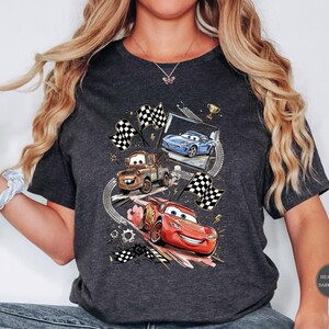 A person wearing a gray t-shirt with a graphic design featuring characters from the animated movie Cars.