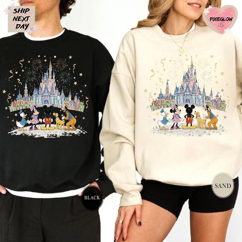 two people wearing matching Disney-themed sweatshirts. The sweatshirt on the left is black and the one on the right is white. Both sweatshirts have a picture of Disney characters and a castle in the background, along with fireworks.