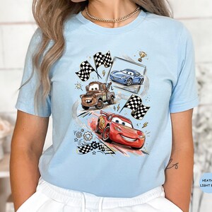 A woman wearing a light blue t-shirt with a graphic of three cartoon cars racing, including a red car, a blue car, and a brown truck.